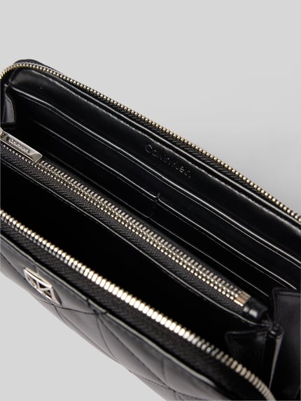 Produktfoto, schwarzes Portemonnaie mit Steppnähten und Label-Applikation von CK Calvin Klein, Hauptfach mit Reißverschluss, Modell 'QUILTED LONG ZIP AROUND', Innenansicht mit mehreren Fächern und glatter, leicht glänzender Textur.