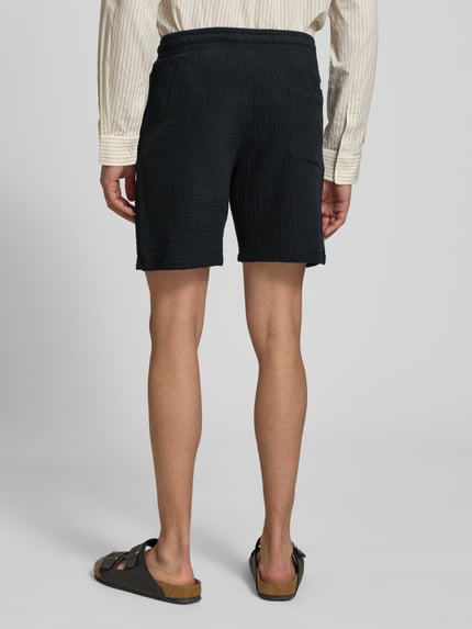 Mannenmodel draagt Shorts met structuurpatroon model 'AIDEN' van Jack & Jones, katoenmix, straight fit, elastische tailleband met trekkoord, zijzakken, zwart, achterkant volledig lichaam, context: taillemaat M 40 cm, binnenbeenlengte M 21 cm.