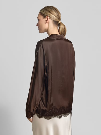 Frauenmodel trägt Relaxed Fit Bluse aus Viskose mit Spitzenbesatz von Jake*s Collection in dunklem Braun, glänzende Oberfläche, Rückenlänge 64 cm, Ärmellänge 55 cm, Reverskragen, V-Ausschnitt, Ganzkörperansicht Rückansicht.