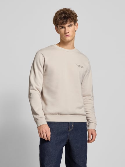Männermodel trägt Sweatshirt mit Label-Print von Jack & Jones aus Baumwoll-Mix, lockerer Schnitt, gerippte Abschlüsse, Rundhalsausschnitt, Rückenlänge 70 cm, Ärmellänge 66 cm; helle Farbe, glatte Textur, Ganzkörperansicht von vorne.