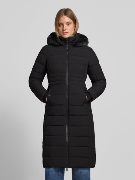 Frauenmodel trägt schwarzen Steppmantel mit Kunstfellkapuze, Zweiwege-Reißverschluss, Slim Fit, NAUTGÅRD 'ECLIPSE', Ganzkörperansicht von vorne.