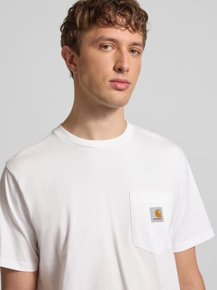 Männermodel trägt Regular Fit T-Shirt mit Logo-Patch von Carhartt Work In Progress in Weiß, reine Baumwolle, Brusttasche, Nahaufnahme Oberkörper.