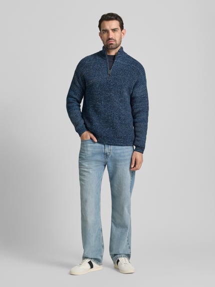 Mannenmodel draagt Relaxed Fit Troyer uit katoen-wolmix MICHAAEL MOULINE van Armedangels in blauwe melange, grofgebreid, label patch, geribde boorden, korte ritssluiting, lange mouwen, volledig lichaamsaanzicht van voren.