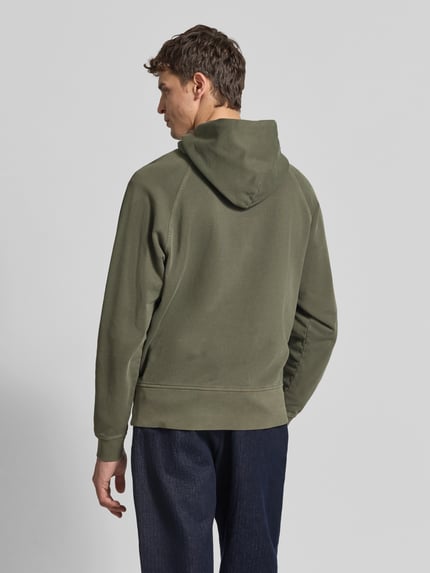 Męski model nosi Regular Fit Hoodie aus reiner Baumwolle von Closed, oliwkowozielony, gładka tkanina, kaptur, krój regular fit, kieszeń kangurka, elastyczne wykończenia, długość pleców w rozmiarze M: 62 cm, pełny widok sylwetki od tyłu.