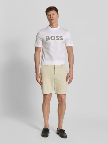 Männermodel trägt Modern Fit Chinoshorts aus Baumwoll-Mix Modell 'KANE1' von BOSS in Beige, unifarben, Ganzkörperansicht von vorne. Herren Chinoshorts, Knopfverschluss, seitliche Eingrifftaschen, Paspeltaschen.