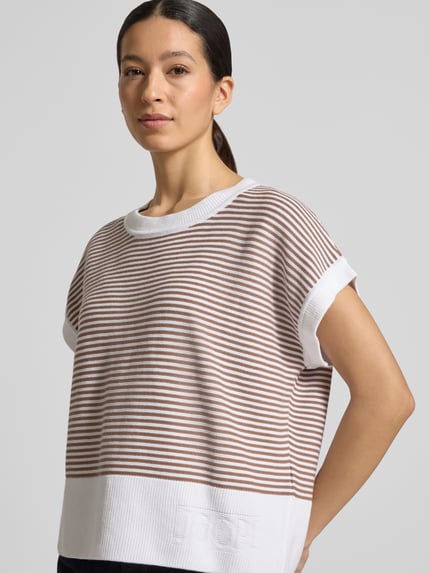 Frauenmodel trägt T-Shirt aus reiner Baumwolle in Strick-Optik Modell 'Kipe' von JOOP!, braun-weiß gestreift, lockere Passform, Rundhalsausschnitt, Label-Detail, Nahaufnahme Oberkörper.