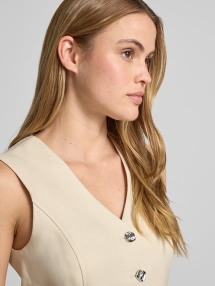 Frauenmodel trägt Weste aus Viskose-Mix mit Knopfleiste Modell 'Esteriane' von MSCH Copenhagen in Beige, strukturierte Oberfläche, Nahaufnahme Oberkörper. Taillierter Schnitt, V-Ausschnitt, Brustweite bei Größe S 41 cm, Schulterbreite 35 cm, Rückenlänge 61 cm.