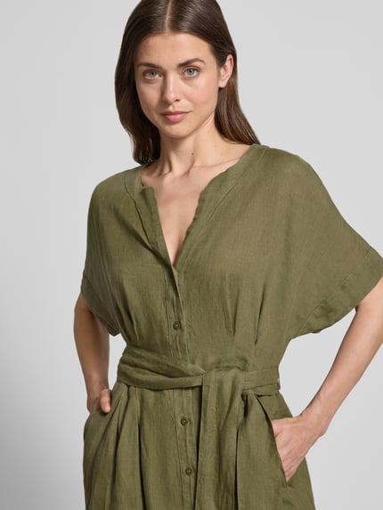 Modelka kobieca nosi Midikleid aus reinen Leinen mit Tunika-Ausschnitt Modell 'Soli' od Christian Berg Woman Selection, oliwkowy kolor, lniana tekstura, taliowany krój, guziki, odpinany pasek, długość pleców w rozmiarze 36: 117 cm, szerokość w rozmiarze 36: 50 cm, długość rękawa w rozmiarze 36: 22 cm; zbliżenie na górną część ciała