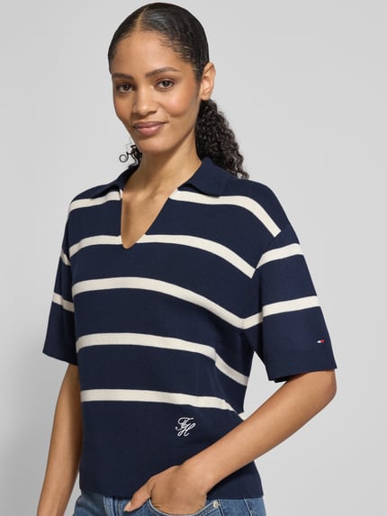 Frauenmodel trägt Regular Fit Pullover aus reiner Baumwolle von Tommy Hilfiger, dunkelblau mit weißen Streifen, Polokragen, V-Ausschnitt, Feinstrick, Logo-Stitching, kurzarm, gerippte Abschlüsse, Ganzkörperansicht von vorne.