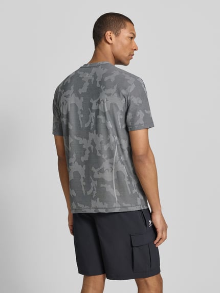 Männermodel trägt T-Shirt mit Rundhalsausschnitt und Label-Detail von EA7 Emporio Armani, Material-Mix mit Stretch-Anteil, Regular-Fit, Rückenlänge bei Größe M 69 cm, graue Camouflage-Optik, Ganzkörperansicht Rückansicht.