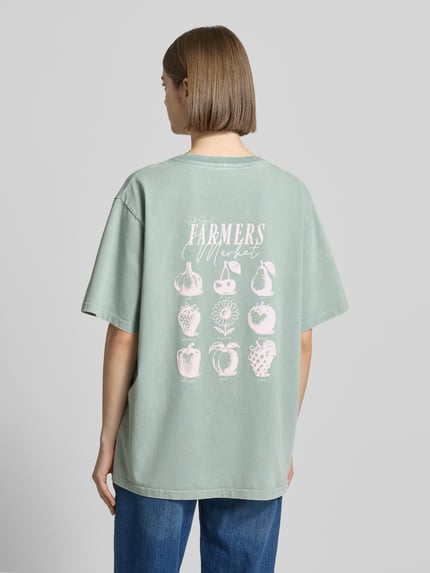 Frauenmodel trägt Damen T-Shirt von OH APRIL aus Reine Baumwolle im Oversized-Stil, Rückenlänge 69 cm, Label-Stitching, Modell 'Farmers Market', Ganzkörperansicht Rückansicht.