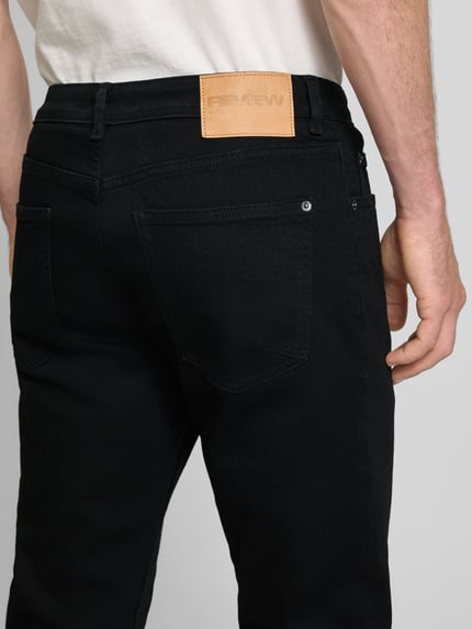 Männermodel trägt schwarze Slim Fit Jeans im klassischen Five-Pocket-Design von REVIEW aus reiner Baumwolle, Detailaufnahme Rückansicht.