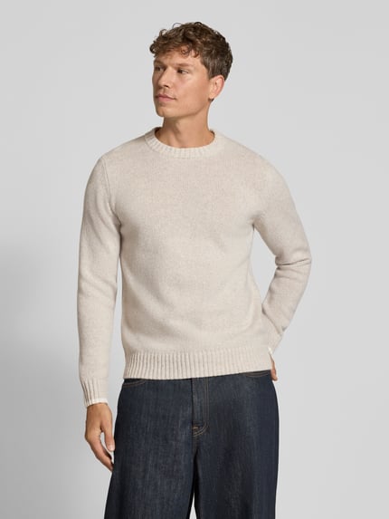 Męski model nosi sweter z dzianiny z czystej żywej wełny z okrągłym dekoltem od MAERZ Muenchen, krój regular fit, długi rękaw, Długość tyłu 65 cm, Długość rękawów 68 cm, jasny beż, tekstura gładka, całkowity widok z przodu