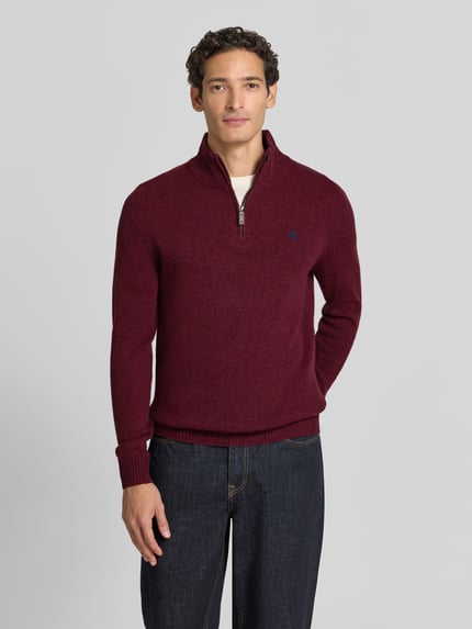 Männermodel trägt Regular Fit Strickpullover aus reiner Wolle von MCNEAL in Bordeaux mit Logo-Stickerei, Troyer-Kragen, Langarm, gerippte Bündchen, Ganzkörperansicht von vorne.