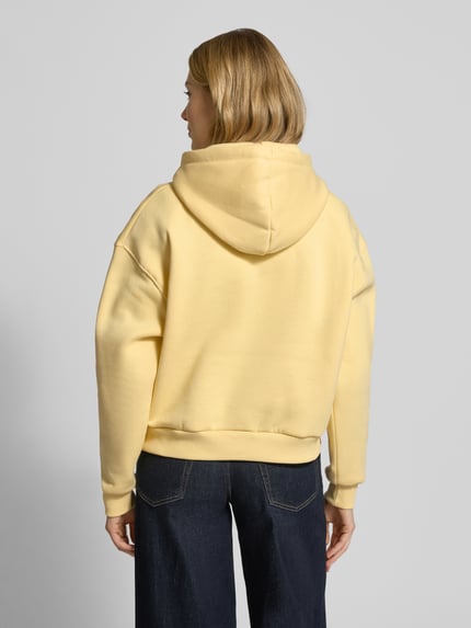 Vrouwenmodel draagt Relaxed Fit Hoodie aus Baumwoll-Mix van Tommy Hilfiger in effen geel, sweatstof, geribde boorden, Ganzkörperansicht Rückansicht.