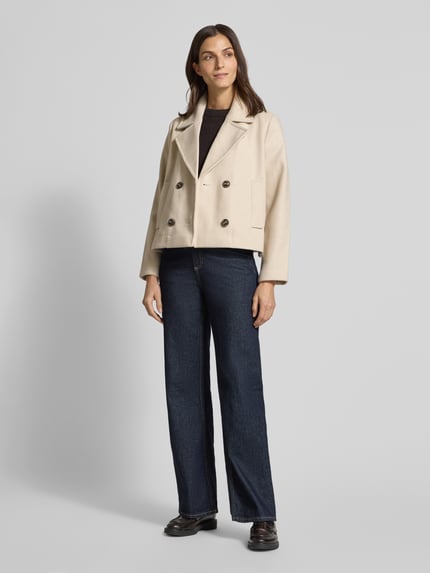 Vrouwenmodel draagt cropped trenchcoat met dubbele knoopsluiting model 'VINCEMIA' van Vero Moda, boxy fit, effen look, geheel vooraanzicht.