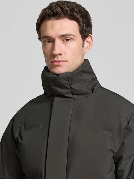 Männermodel trägt Regular Fit Steppmantel mit Steekzakken van Lindbergh in donkergroen, gladde textuur, Nahaufnahme Oberkörper. Heren gewatteerd jack, regular fit, capuchon, verborgen ritssluiting, steekzakken, ruglengte maat M 110 cm, schouderbreedte 46 cm, borstwijdte 57 cm, mouwlengte 66 cm.