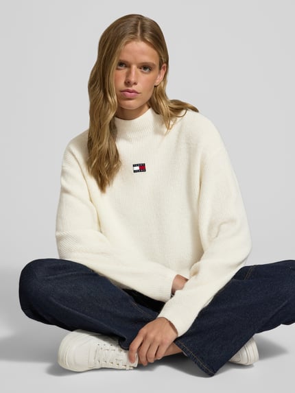Frauenmodel trägt weißen Relaxed Fit Pullover mit Alpaka-Anteil von Tommy Jeans, kombiniert mit blauer Jeans, Nahaufnahme Oberkörper. Damen Pullover von Tommy Jeans.