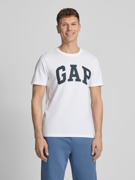 Männermodel trägt T-Shirt mit Logo und Rundhalsausschnitt von GAP aus reiner Baumwolle, Regular-Fit, weiß-blau, Ganzkörperansicht von vorne. Rückenlänge bei Größe M: 72 cm.