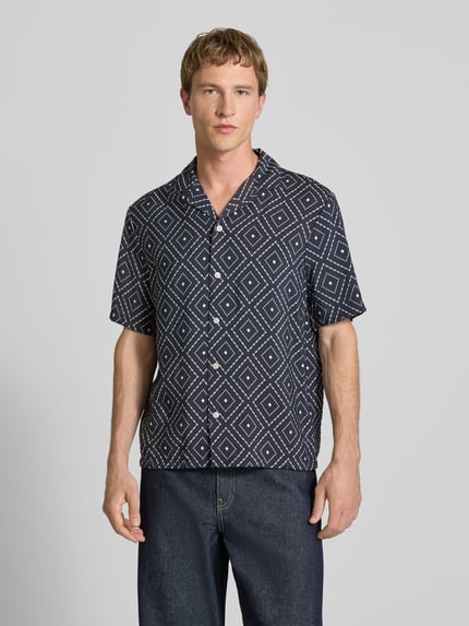 Männermodel trägt Modern Fit Freizeithemd aus Viskose-Mix mit Reverskragen von REVIEW, schwarz mit geometrischem Muster, Nahaufnahme Oberkörper.