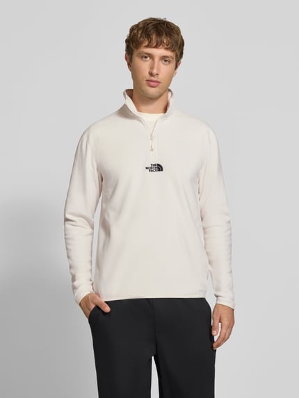 Männermodel trägt Fleecepullover mit Label-Stitching von The North Face in Creme, Stehkragen, Reißverschluss, Regular Fit, Ganzkörperansicht von vorne.