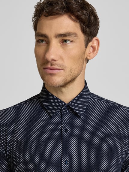 Männermodel trägt Slim Fit Businesshemd mit Allover-Muster Modell 'HANK' von BOSS, Kentkragen, Nahaufnahme Oberkörper.