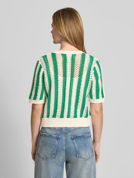 Frauenmodel trägt Cropped Cardigan mit Lochmuster Modell 'Siva' von Lollys Laundry im Baumwoll-Mix, Strick-Optik, Halbarm, grün-creme Farben, Knopfleiste, elastische Abschlüsse, Rückenlänge bei Größe S 51 cm, Ärmellänge 27 cm, Ganzkörperansicht Rückansicht.