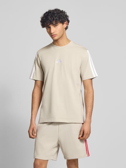 Mannelijk model draagt Regular Fit T-Shirt uit puur katoen van adidas Sportswear, look: effen, regular fit, logoprint, contraststrepen, ronde hals, korte mouw; Ganzkörperansicht van voren.
