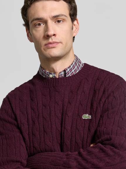 Mannenmodel draagt Regular Fit Pullover aus reiner Wolle van Lacoste in donkerrood met kabelmotief en zachte textuur, Nahaufnahme Oberkörper.