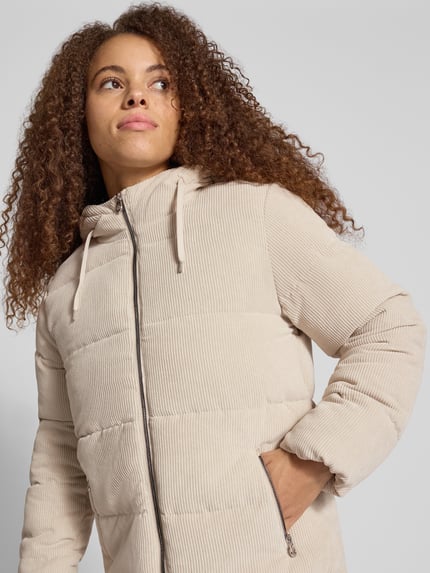 Frauenmodel trägt Steppmantel mit Kapuze Modell 'ONLDOLLY' von ONLY in Beige, Cordstruktur, Kordeln, Reißverschlusstaschen, Nahaufnahme Oberkörper.