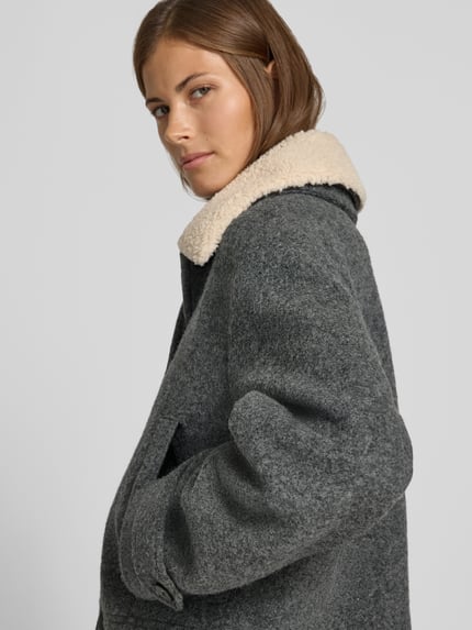 Frauenmodel trägt Jacke mit Kentkragen und Eingrifftaschen von Style Icon Collection in Grau, wollige Textur, Nahaufnahme Oberkörper. Gerader Schnitt, sichtbarer Kentkragen mit heller Struktur, seitliche Eingrifftaschen und Knopfleiste, Kontext: Größe 36, Rückenlänge 54 cm, Schulterbreite 52 cm, Brustweite 50 cm, Ärmellänge 60 cm.