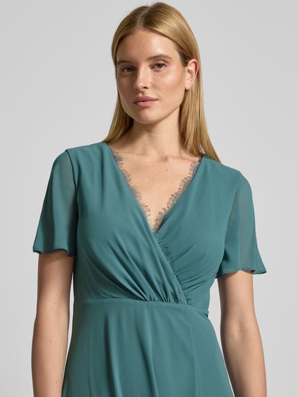 Frauenmodel trägt Damen Abendkleid mit Spitzenbesatz von Christian Berg Cocktail in Türkis, V-Ausschnitt, Wickel-Optik, Nahaufnahme Oberkörper.