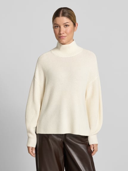 Modelka kobieca ma na sobie Strickpullover aus Schurwolle mit Stehkragen od windsor., kolor ecru, gruby splot, prosty krój relaxed fit, długość tyłu 59 cm, długość rękawa 57 cm, miękka faktura, zdjęcie całego ciała z przodu.