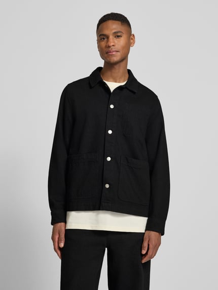 Männermodel trägt Regular Fit Overshirt mit Brusttasche Modell 'Layton' von Les Deux, Reine Baumwolle, Kentkragen, Knopfleiste, Eingrifftaschen, Sportmanschetten, schwarze Farbe, glatte Textur, Ganzkörperansicht von vorne.
