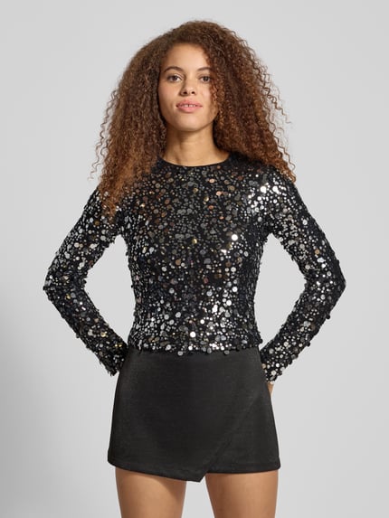 Frauenmodel trägt schimmerndes Slim-Fit Langarmshirt mit Paillettenbesatz Modell 'CATINA' von Only in glänzender Mesh-Optik, Ganzkörperansicht von vorne.