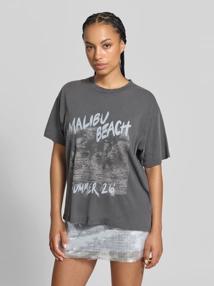 Frauenmodel trägt Relaxed Fit T-Shirt aus reiner Baumwolle von Anine Bing, dunkelgrau mit Statement-Print und Rundhalsausschnitt, Ganzkörperansicht von vorne.