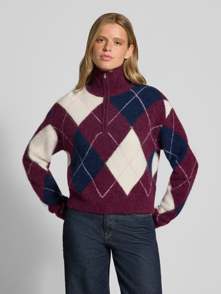 Frauenmodel trägt Regular Fit Pullover aus Alpaka-Woll-Mix von Tommy Jeans in Lila, Weiß und Dunkelblau, Rautenmuster, Nahaufnahme Oberkörper. Damen Pullover von Tommy Jeans.