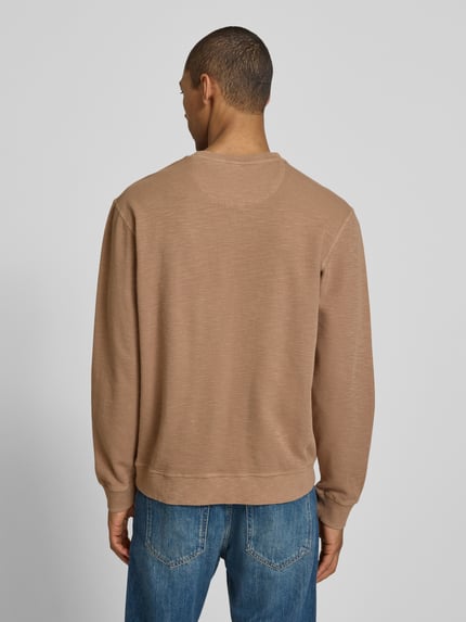 Männermodel trägt Regular Fit Sweatshirt mit Rundhalsausschnitt von Scotch & Soda in beige aus katoenmix mit labeldetail, ruglengte maat M 68 cm, mouwlengte maat M 65 cm, ganzlichaamsaanzicht van achteren.