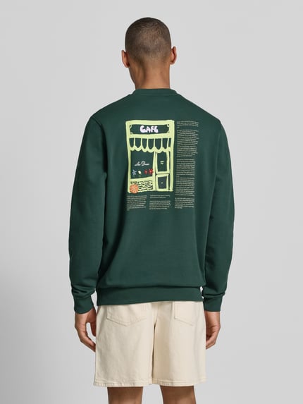 Männermodel trägt Sweatshirt mit Label-Details und Rundhalsausschnitt von Les Deux im Baumwoll-Elasthan-Mix, Regular-Fit, Rückenlänge 66 cm, Ärmellänge 70 cm, dunkelgrün mit grafichem Print, Ganzkörperansicht Rückansicht.