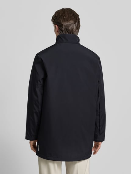 Männermodel trägt Trenchcoat mit Stehkragen von ARMANI EXCHANGE in Dunkelblau, gerader Schnitt, Rückenansicht Ganzkörperansicht.