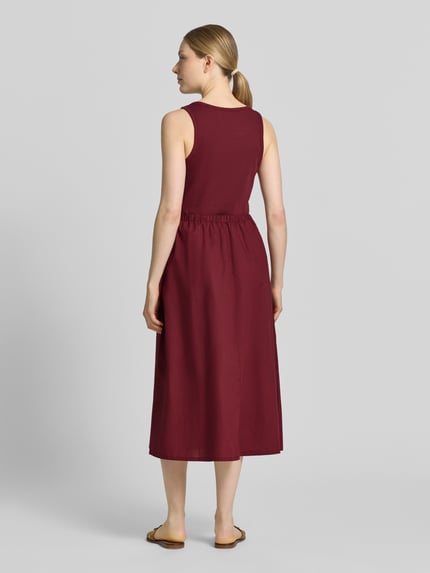Modelka nosi Fit and Flare Freizeitkleid aus reiner Baumwolle od s.Oliver RED LABEL, ciemnoczerwony kolor, gładka tekstura, widok całej sylwetki z tyłu.