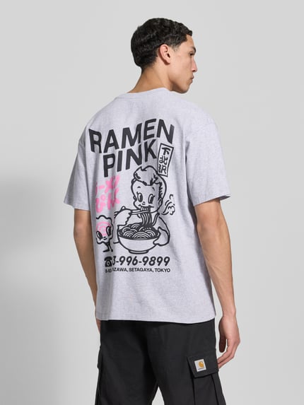 Männermodel trägt T-Shirt aus katoen model 'RAMEN PINK' van Edwin, rechte fit, lichtgrijs met zwarte en roze print, ganzkörperansicht rückansicht.