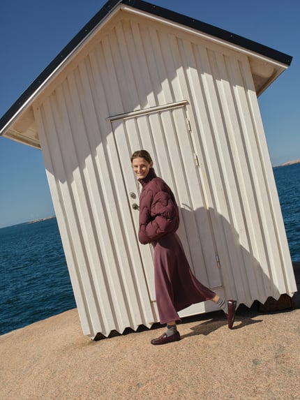 Vrouwenmodel draagt Midirok met elastische band van Christian Berg Woman in elastische materiaalmix met modal, los model, midilengte, bandwijdte maat S 80 cm, bruinpaars op rotsen aan het water, volledige lichaamsvoorzijde.
