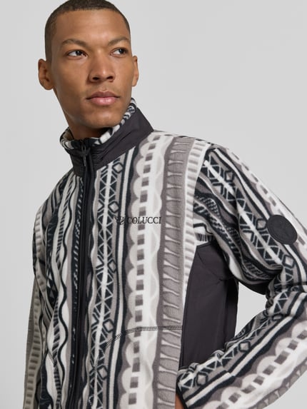 Männermodel trägt Regular Fit Fleecejacke mit Stehkragen Modell 'SIGNATURE' von COLUCCI, grafisches Muster in Schwarz, Grau und Weiß, Logo-Stitching, Nahaufnahme Oberkörper.