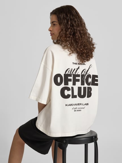 Frauenmodel trägt Cropped Oversized T-Shirt mit Label-Print von Karo Kauer in Creme mit schwarzem Aufdruck, reine Baumwolle, Ganzkörperansicht Rückansicht.