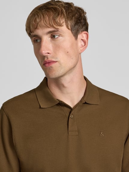 Męski model nosi Slim Fit Poloshirt mit Label-Stitching Modell 'AUSTIN' von JACK & JONES, mieszanka materiałów z bawełną, kołnierzyk polo, wyhaftowane logo, długość tyłu w rozmiarze M: 70 cm, zbliżenie na górną część ciała.