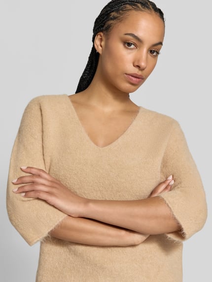 Frauenmodel trägt Wollpullover aus Alpaka-Woll-Mix von Juvia in Beige, Strick-Optik, V-Ausschnitt, 3/4-Arm, lockere Passform, Nahaufnahme Oberkörper.