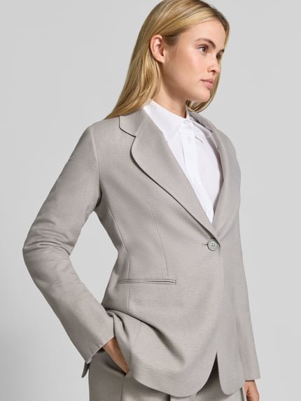 Frauenmodel trägt Blazer mit Reverskragen und Brustleistentasche von Emporio Armani in Hellgrau, Material-Mix, Nahaufnahme Oberkörper.