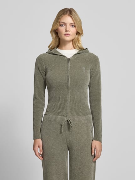 Frauenmodel trägt Sweatjacke mit Kapuze Modell 'MAYA KNIT HOODIE' von Juicy Couture in unifarbener Strickoptik, cropped geschnitten, mit Reißverschluss, Logo-Stitching, gerippten Abschlüssen und Kapuze, Ganzkörperansicht von vorne.