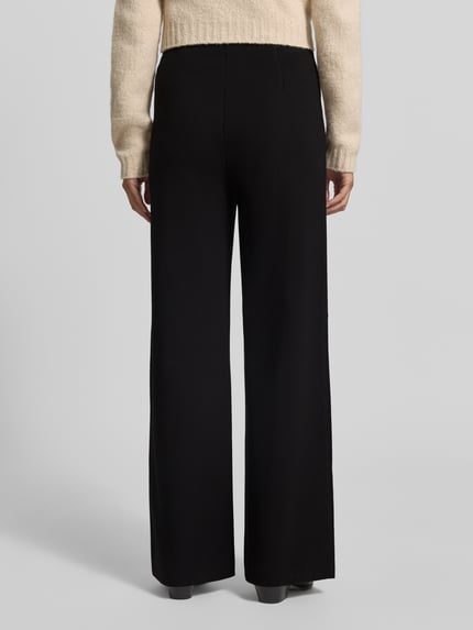 Frauenmodel trägt Flared Cut Hose mit elastischem Bund und Längsnähten von Christian Berg Woman Selection, schwarze Farbe, glatte Textur, Ganzkörperansicht Rückansicht. Viskose-Mix mit Stretch-Anteil, Längsnähte sichtbar, Bundweite 39 cm, Innenbeinlänge 81 cm.